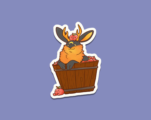 Illustration of a cute, fluffy Harvest Moon Jackalope sitting inside a wooden barrel, with small red apples scattered around. The rabbit has a playful expression, its ears perked up and paws resting on the rim of the barrel, creating an adorable, cozy scene.