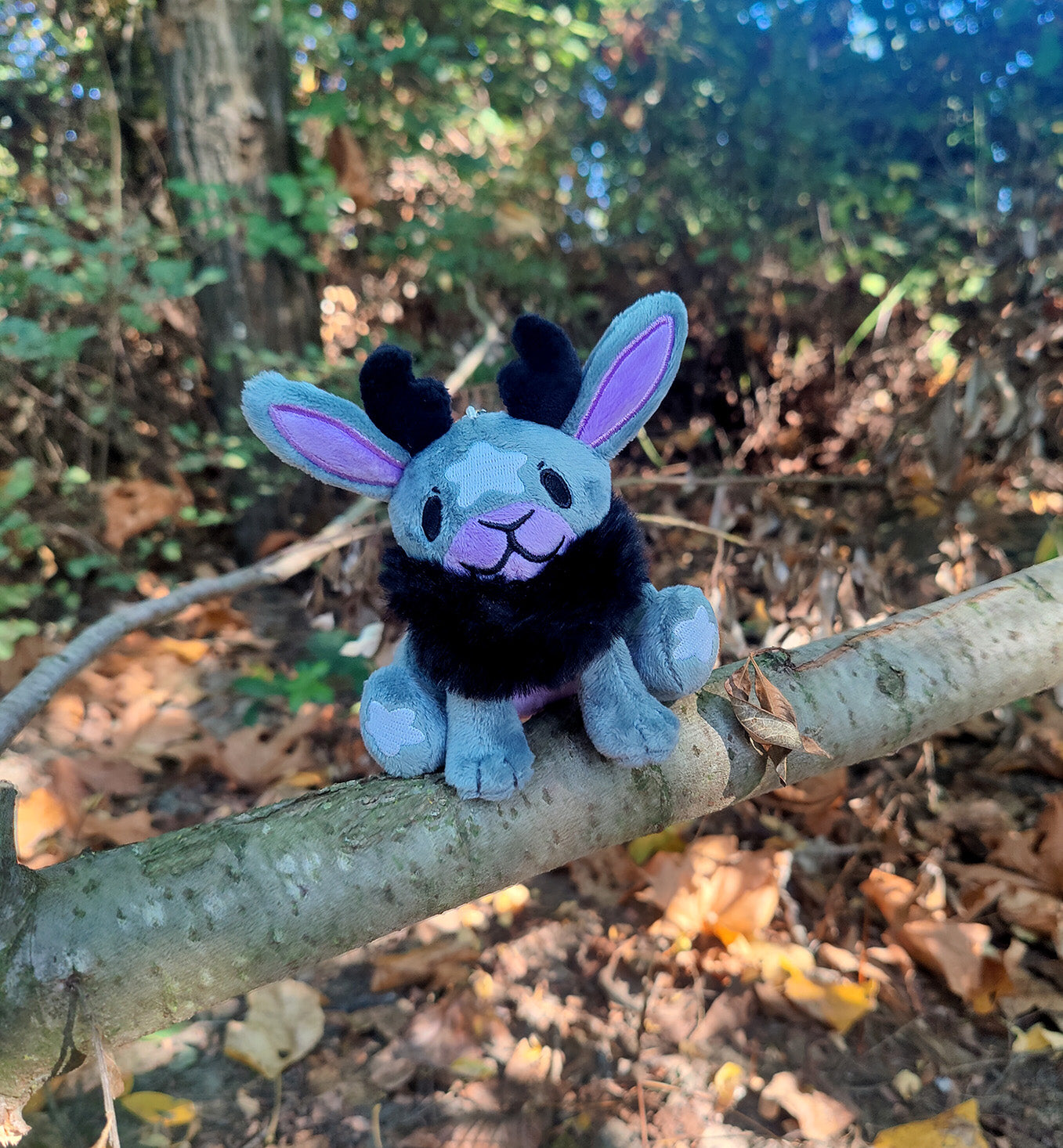 Plush toy resembling Jackalope with purple/black accents on a tree branch in a forest setting